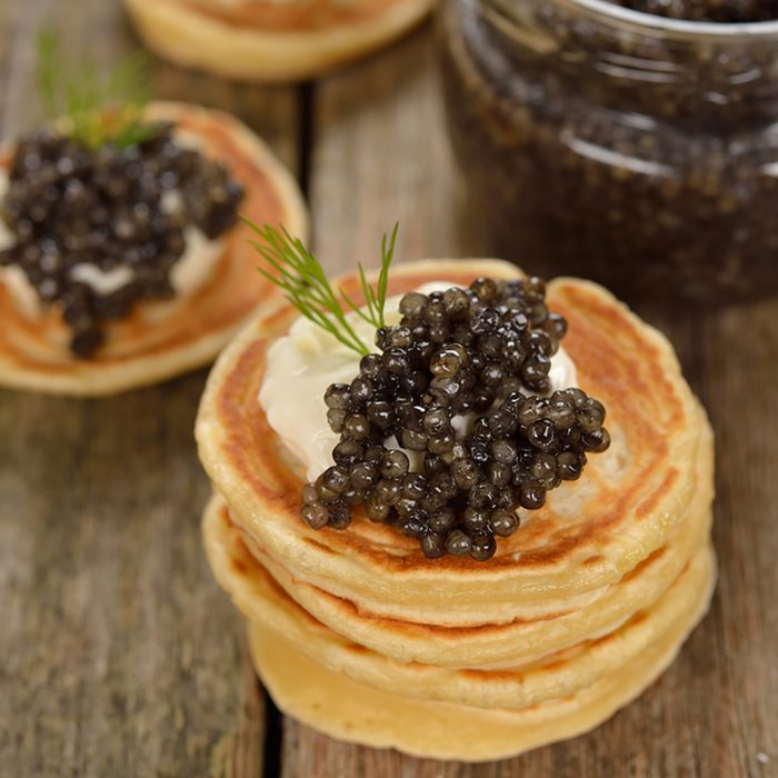 Mini pancakes with black caviar on a wooden background; Shutterstock ID 351283835