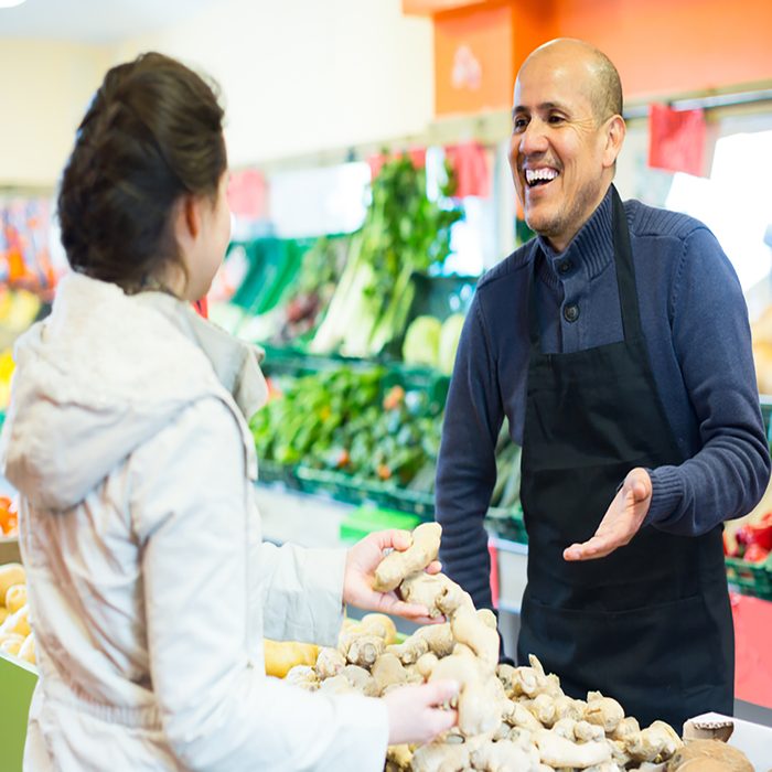friendly salesman helping female customer to choose ginger in supermarket