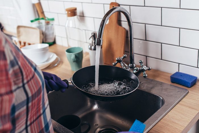 Young woman wearing rubber gloves washing frying pan in kitchen