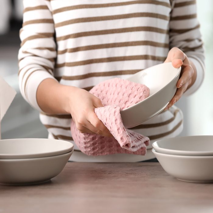 Woman wiping dishware with cotton towel in kitchen.