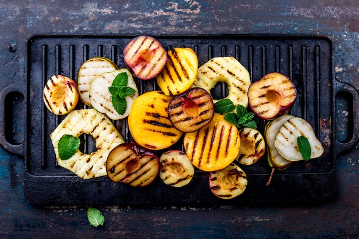 Grill fruits - pineapple, peaches, plums, avocado, pear on black cast iron grill board