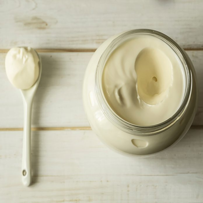 Mayonnaise in a glass jar with a spoon on white wooden boards.