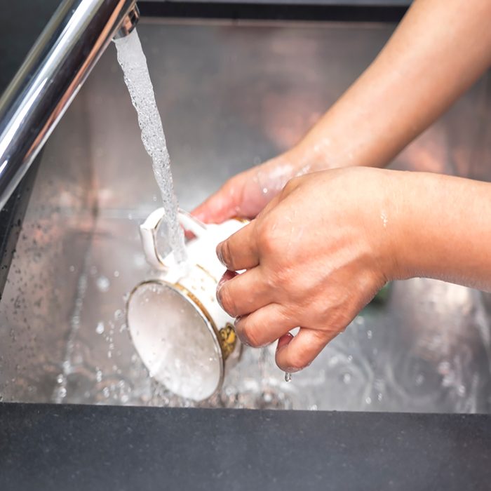 Women's hands wash dishes in the kitchen sink.