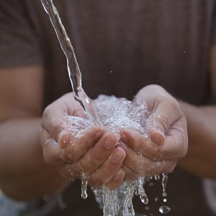 A man catches running water in his cupped hands outdoors.