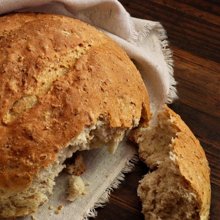 Freshly baked multi-grain bread with homespun fabric on rustic dark wood background.