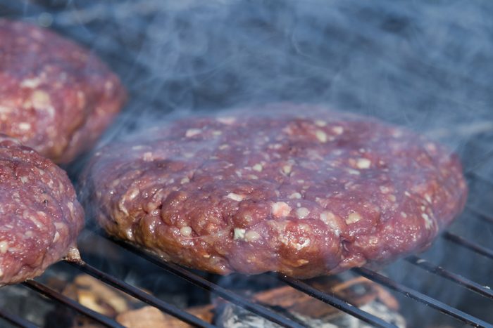 close up of hand formed hamburger patties on an outdoor grill with hickory wood chips for a smoky flavor