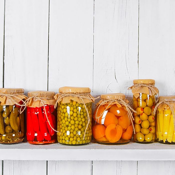 Preserved food in glass jars, on a wooden shelf. Various marinaded food