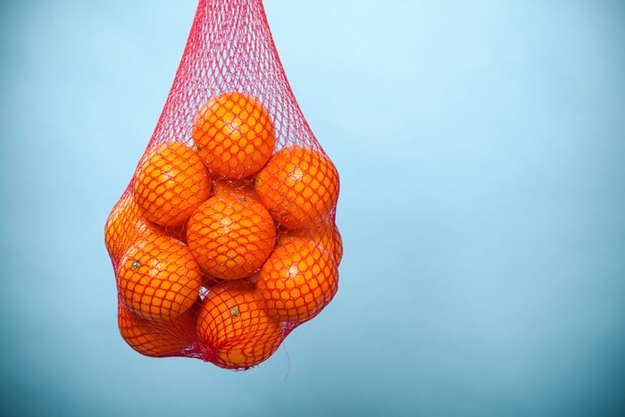 Mesh bag of fresh oranges healthy tropical fruits from supermarket on blue.