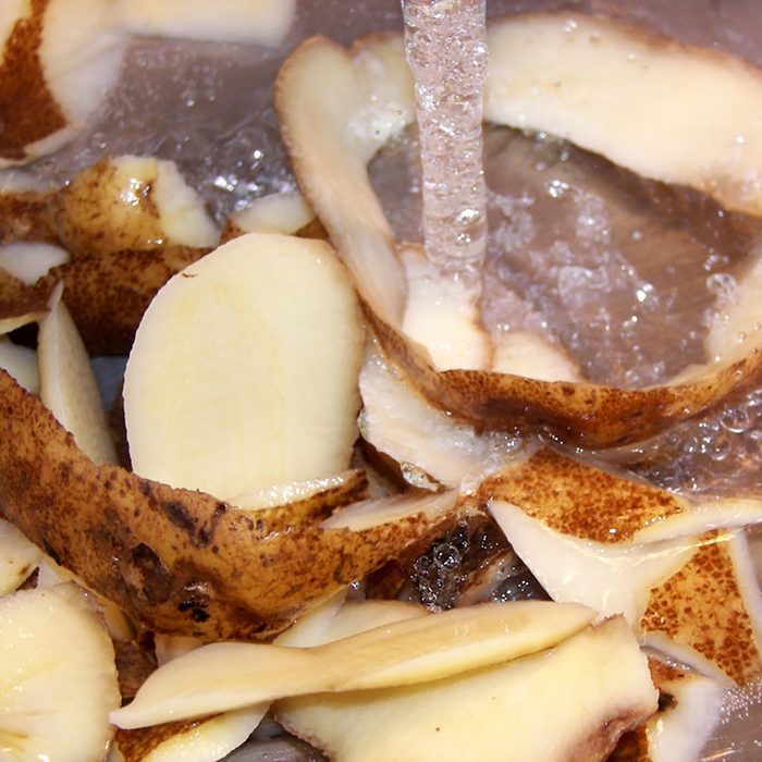 raw potato peelings in kitchen sink with stream of water from faucet