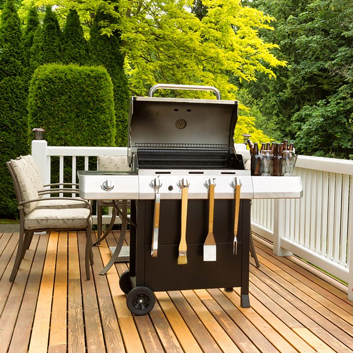 Photo of a clean barbecue cooker with cookware and cold beer in bucket on cedar wood patio. Table and colorful trees in background.