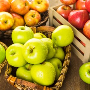 Variety of organic apples in baskets on wood table