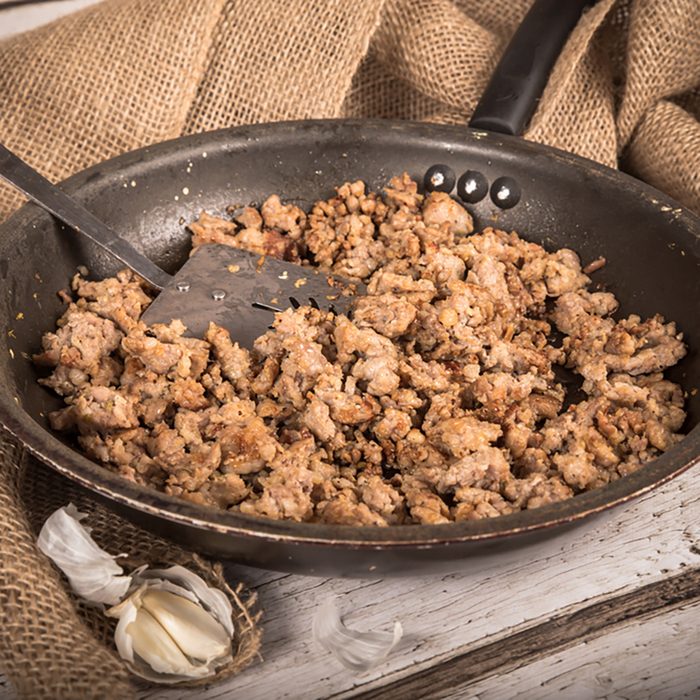 Cooking Ground sausage meat in frying pan with garlic and burlap background