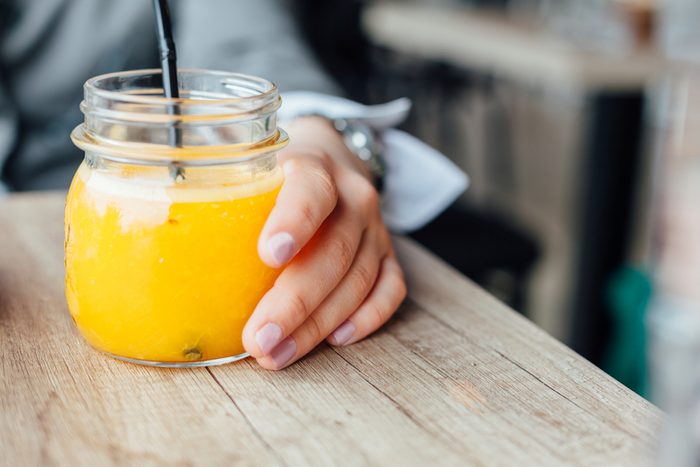 Bottle of freshly squeezed orange. Woman drinking orange juice in a cafe