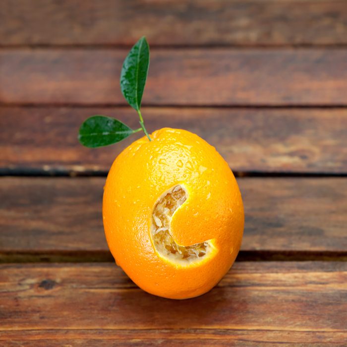 Fresh orange with letter C cut into it resembling vitamin C placed on wooden table.