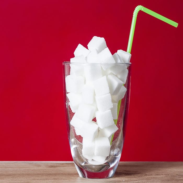 Glass with straw full of sugar and sugar cubes on red background
