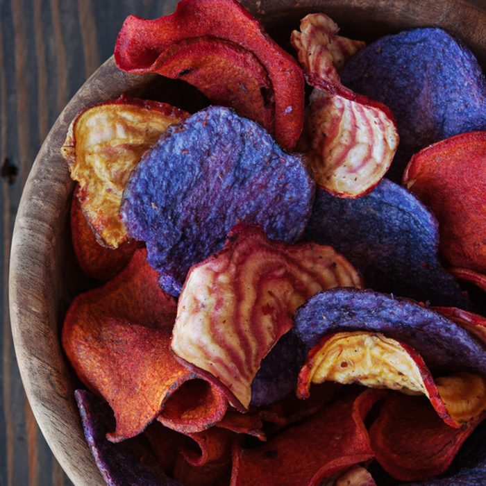 Crunchy organic dry potatoese chips and beetroot chips served as a finger food snack in a wooden bowl