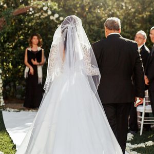 Look from behind at father leading bride in luxuriant wedding dress to altar