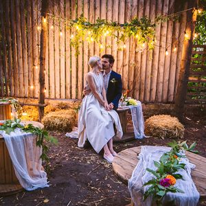 Beautiful young casual couple in love, sitting at wooden table. Wedding location is at country style garden with American lighting and simple trend decor