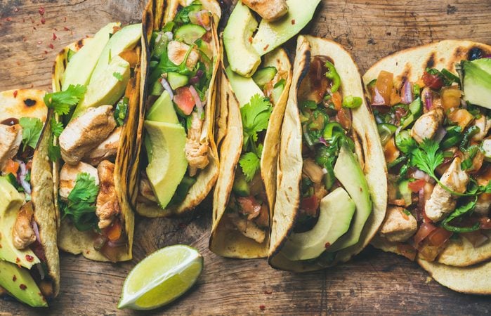 Tacos with grilled chicken, avocado, fresh salsa sauce and limes over rustic wooden background