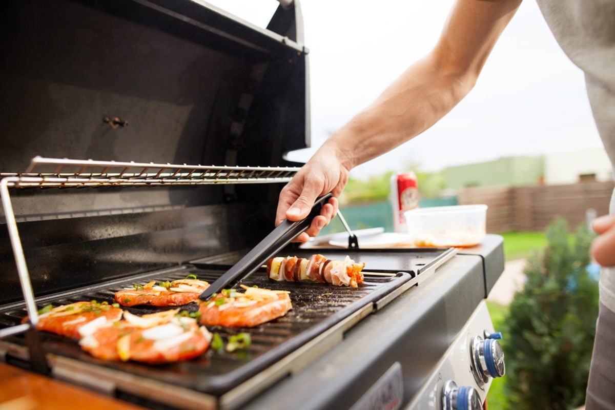 Hand of young man grilling some meat and vegetable-meat skewers on huge gas grill