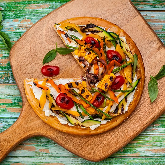 Delicious summer appetizer: Vegetarian pizza with grilled vegetables and soft cheese on wooden board. Top view