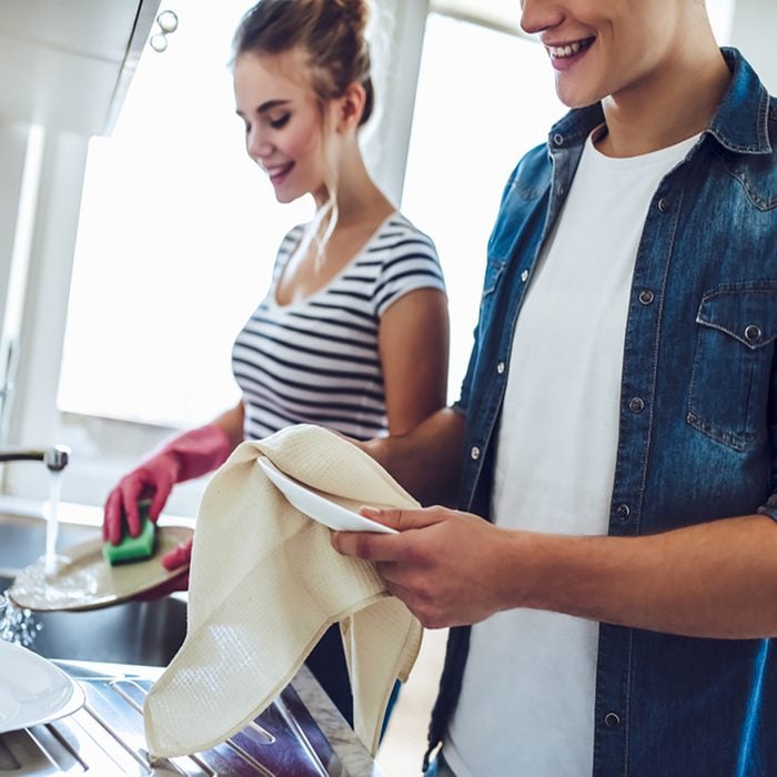 Cropped image of young happy couple is washing dishes while doing cleaning at home.