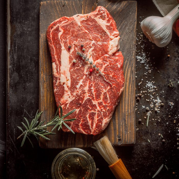 Close up Wooden Chopping Board with Raw Beef Meat on a Rustic Table with Herbs and Spices