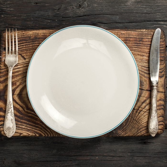 White empty plate with fork and knife on a old wooden board on a dark wooden background