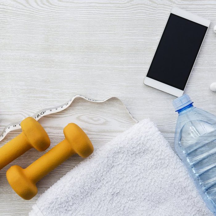 Towel, water bottle, phone and dumbbells spread out on the floor 