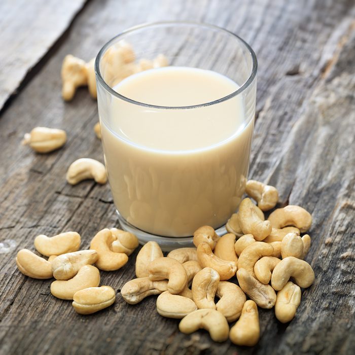 Heap of raw cashews and a glass of cashew milk, on wooden surface