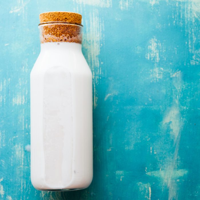 Top view of an Homemade coconut milk in a bottle, made after mixing coconut and water in a blender and pressed through a cotton sieve, over a rusty blue background
