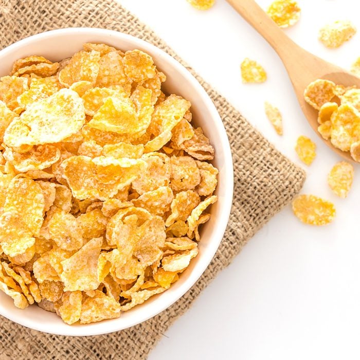 bowl of cornflakes and cornflakes on wooden spoon over a sackcloth on white table background, Top view with copy space; Shutterstock ID 492732964; Job (TFH, TOH, RD, BNB, CWM, CM): Taste of Home