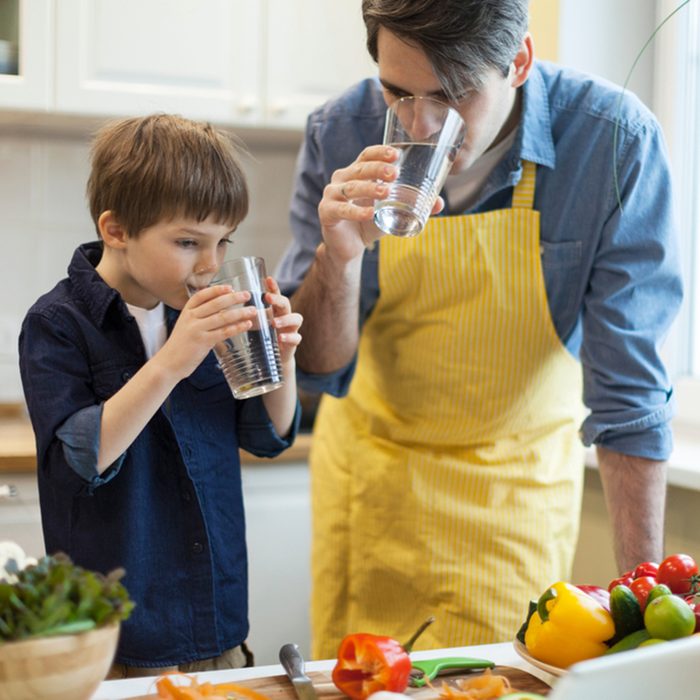 Father and son cooking healthy food in the kitchen and drinking water