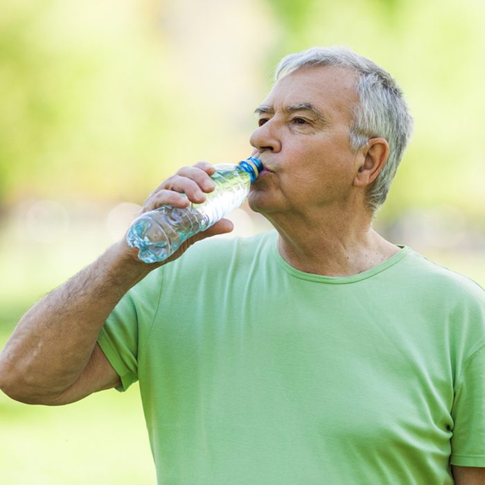 Senior man is drinking water after workout in park.