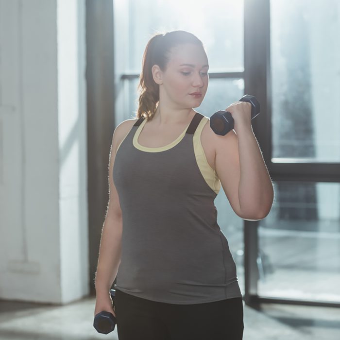 Curvy girl lifting dumbbells in gym