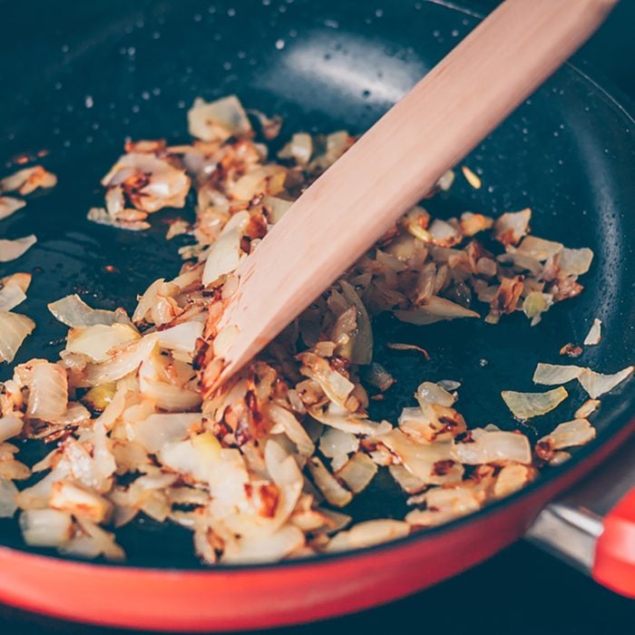 The cook stirs fried onions in a frying pan