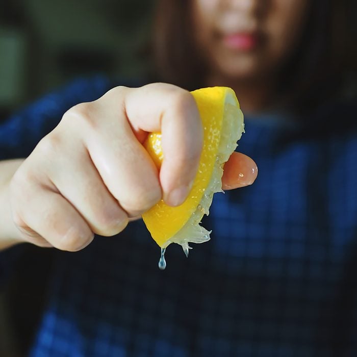 Woman hand squeezing a lemon half on blurred background of her blue plaid or tartan blouse.