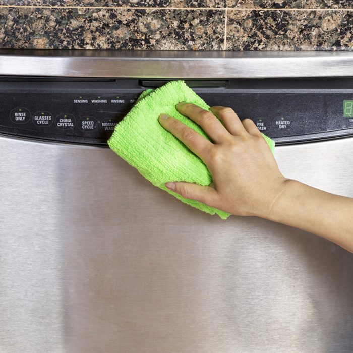 Female hand wiping down front part of stainless steel dishwasher with microfiber towel