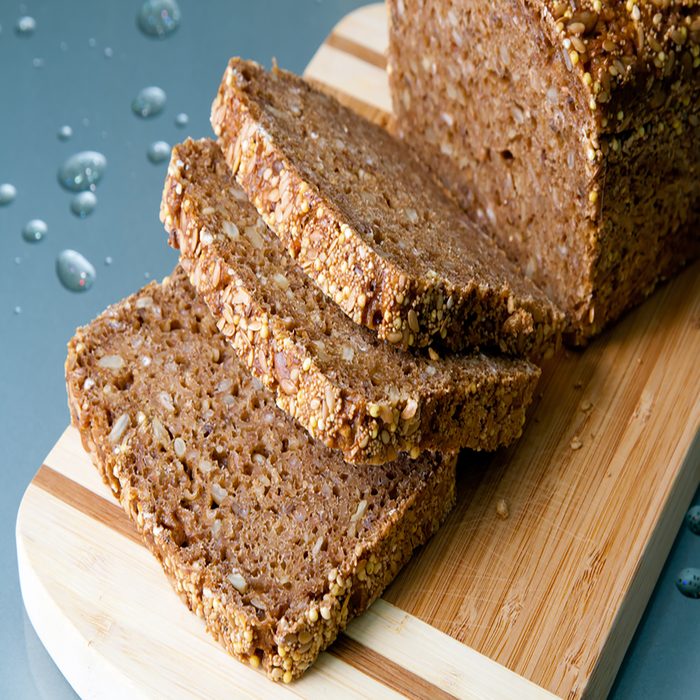 Loaf of wholegrain bread and slices on wooden cutting board.