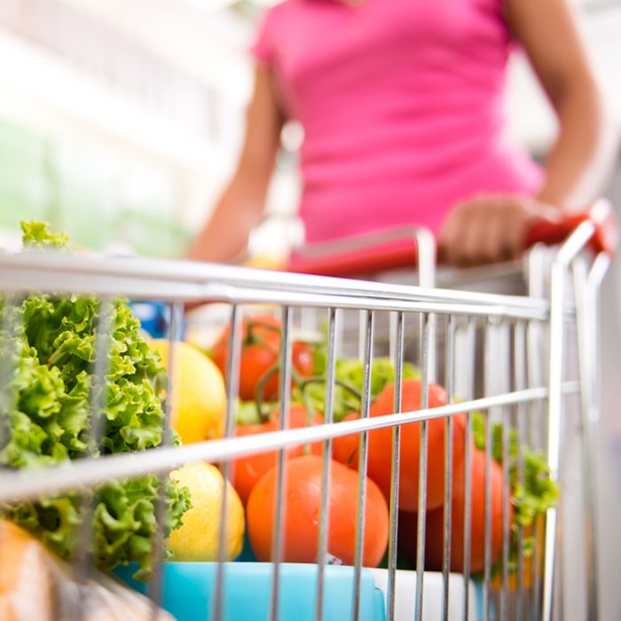 Woman at supermarket pushing a shopping cart filled with fresh fruit and vegetables.