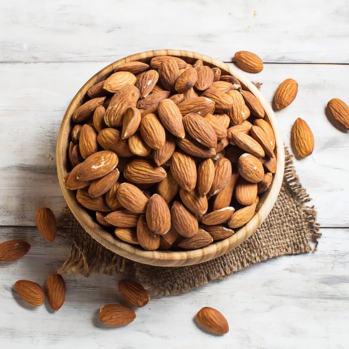 Almonds in brown bowl on wooden background