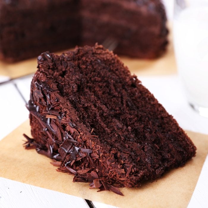 Sliced tasty chocolate cake on sheet of parchment and glass of milk on wooden table background