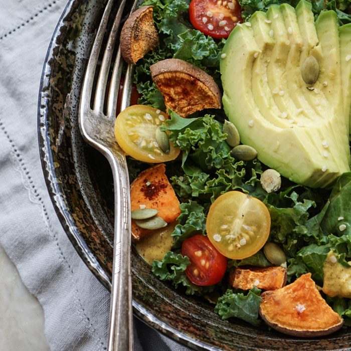 Kale, roasted yams and avocado salad on stone background