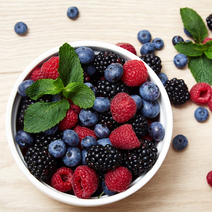 Beautiful juicy ripe natural organic raspberries blackberries blueberries and mint blue tablecloth dots white dish heart shape