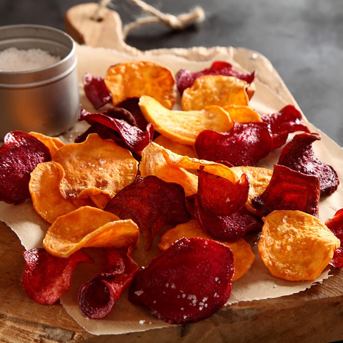 Crisp crunchy organic vegetable chips with fried or oven-baked potato and beetroot chips served as a finger food snack on a wooden chopping board with sea salt and copyspace