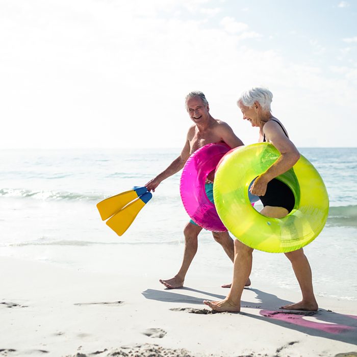 Happy senior couple walking on beach with inflatable rings and flippers on a sunny day; Shutterstock ID 398324230