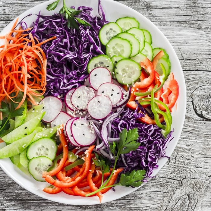 Fresh vegetable salad with red cabbage, cucumber, radish, carrots, sweet peppers, red onion and parsley on a white plate.