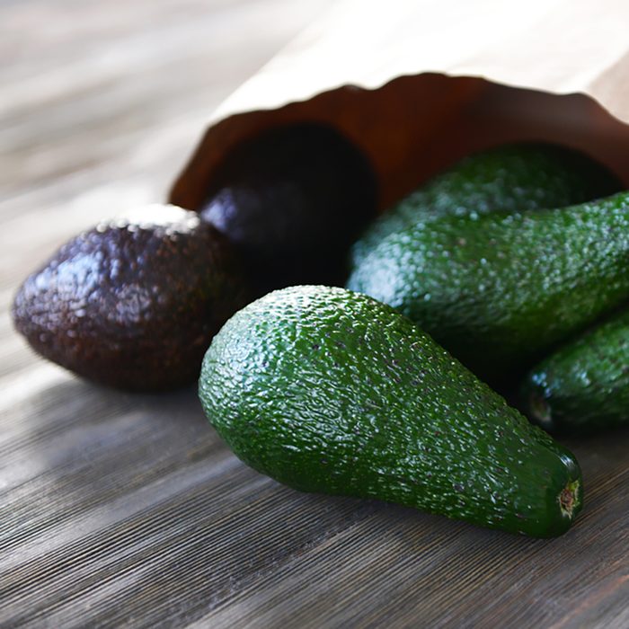 Fresh avocados in paper bag on wooden background;