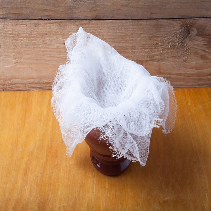 Clay pot with ghee under cheesecloth on light wooden table. 