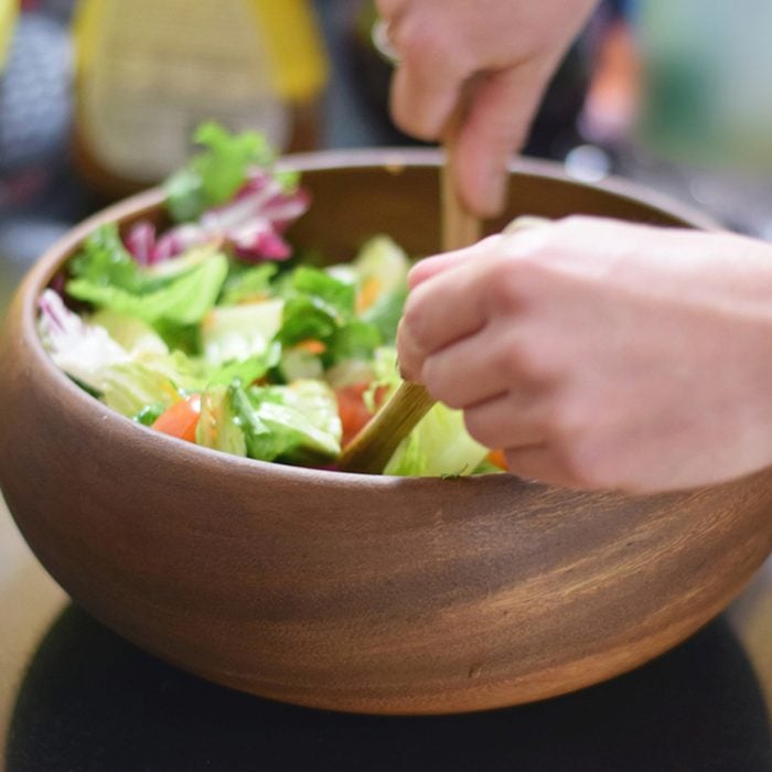 Healthy green salad being tossed in wooden bowl on counter